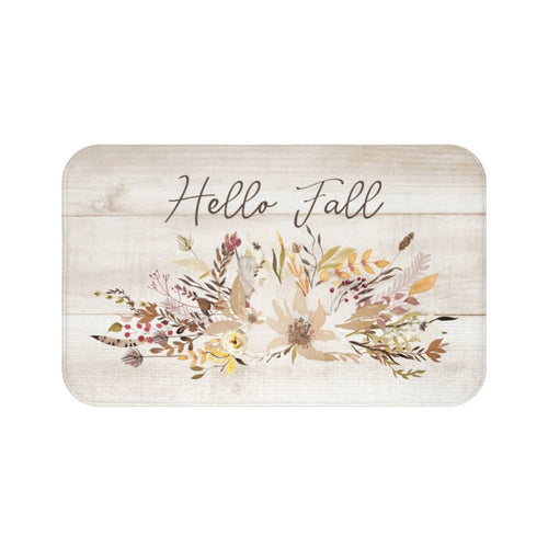 A rectangular memory foam mat with a 'Hello Fall' text in cursive script and a floral design featuring autumn-colored leaves and flowers against a background of light sand colored wood planks.