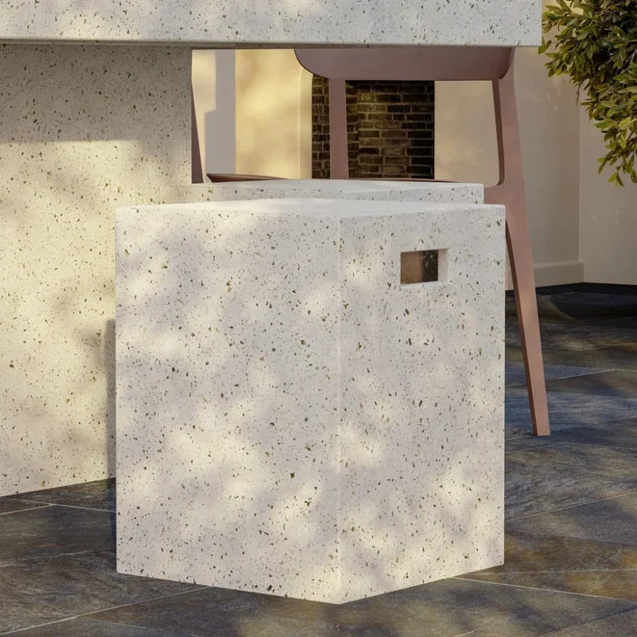 White speckled concrete outdoor stool beside a beige chair on a dark tiled floor with some greenery visible