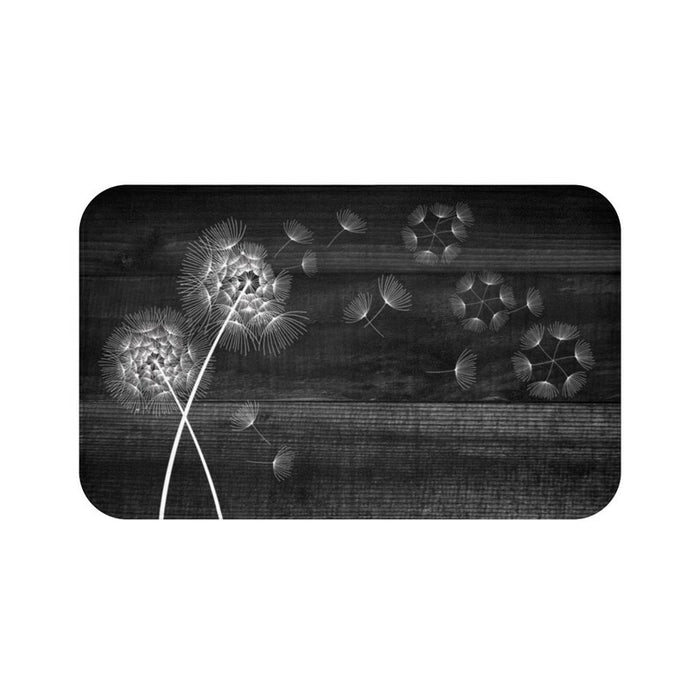 This is an image of a rectangular floor mat with rounded corners. The background of the mat mimics distressed, black-colored wooden planks. The horizontal plank lines give the mat a texture and farmhouse feel. The primary graphic is a cluster of stylized dandelion seed heads on the left side. The seed heads are drawn in fine detail, and several dandelion seeds are shown floating across, suggesting a gentle breeze.